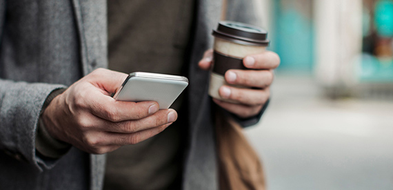 Man holding phone and coffee.